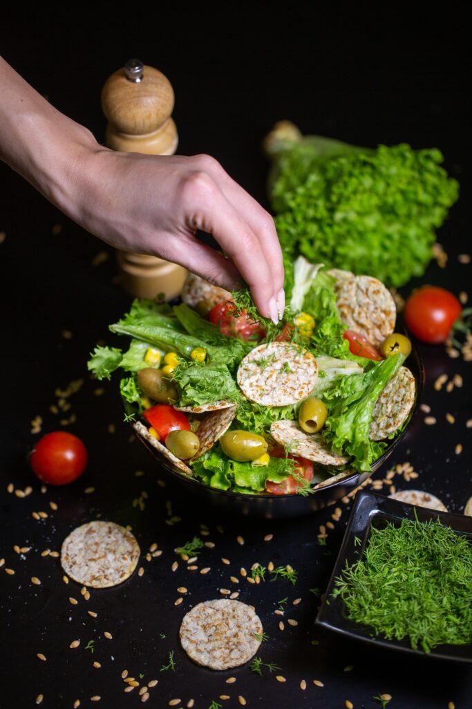 vertical closeup of a person putting herbs on salad in a bowl on the table under the lights