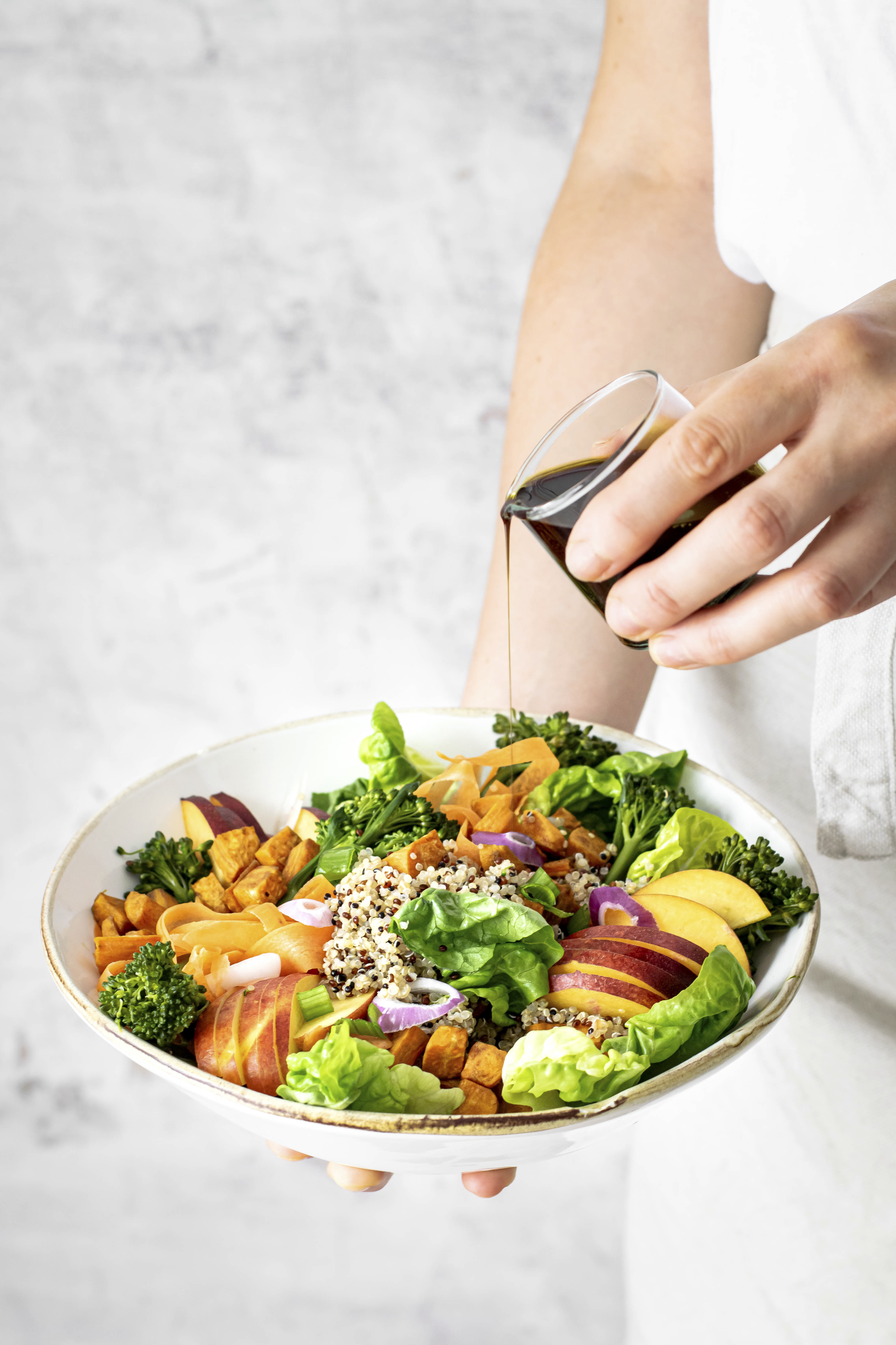 woman pouring pumpkin seed oil over sweet potato buddha bowl